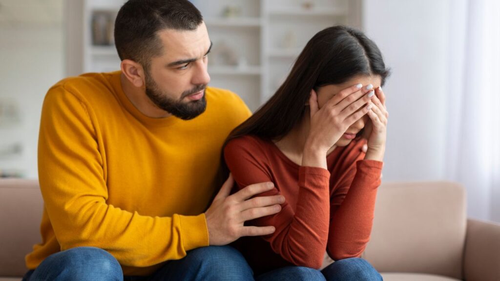 Una persona che chiede scusa sinceramente al partner con uno sguardo empatico, entrambi seduti sul divano, luce soffusa, espressioni emozionate – stile semi-realistico